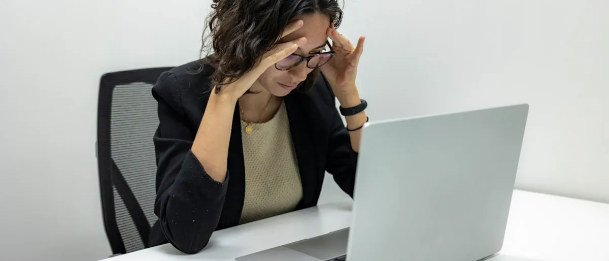 A frustrated woman holding her head while looking at a laptop screen