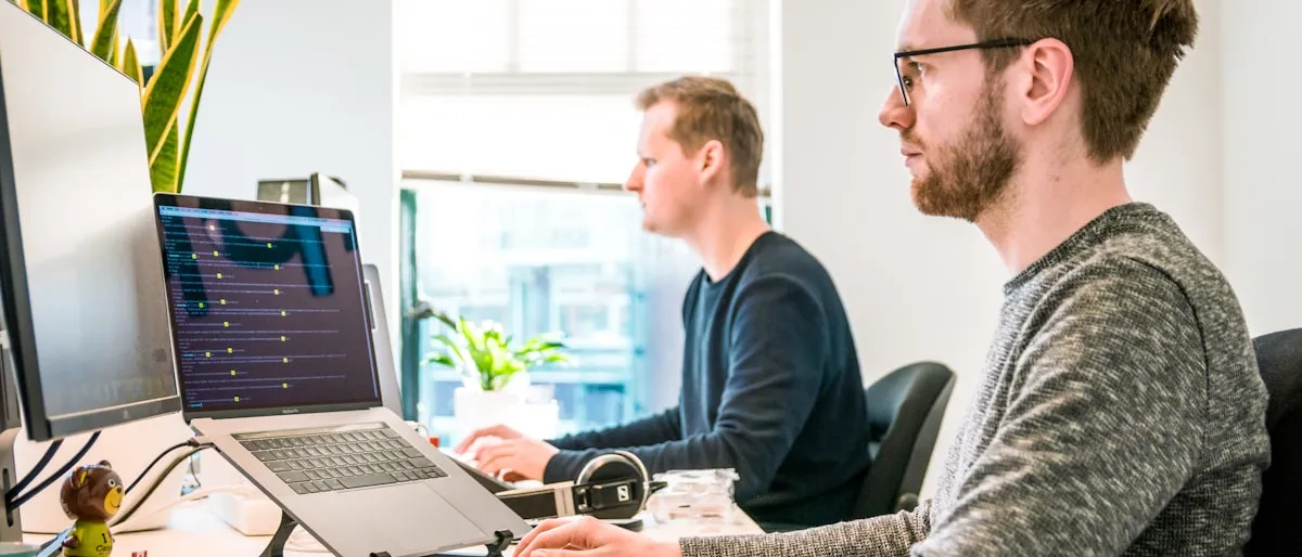 Two coworkers sitting side by side, each working on their own computer