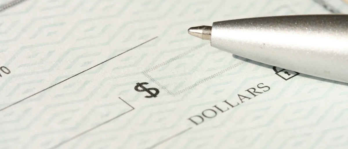 Close-up of a pen resting on a blank paycheck near the dollar amount line